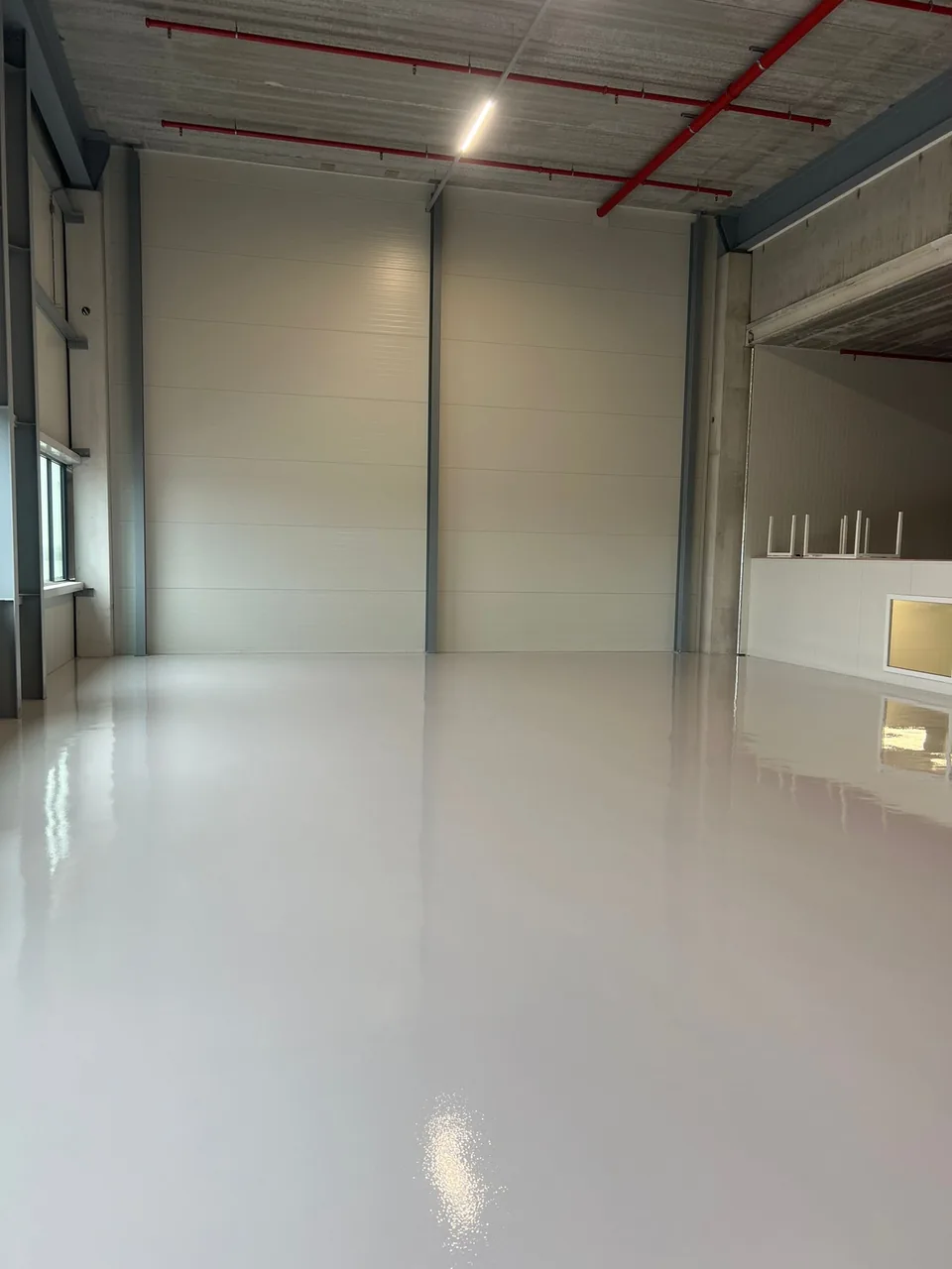 Seamless grey epoxy resin floor in a new industrial hall with wall panels and an overhead door