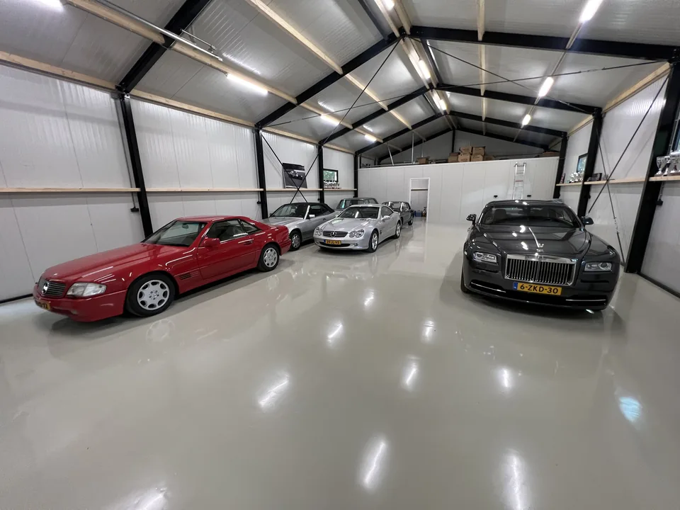 Light epoxy resin floor in a garage with classic sports cars beneath a timber roof structure