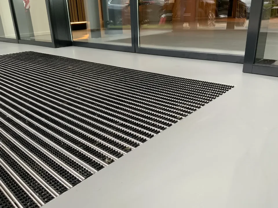 Aluminium entrance mat set flush into the Comforpur 635 Betonlook resin floor at an entrance with a glazed facade