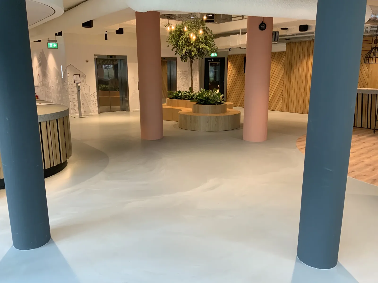 Light grey Comforpur 635 Betonlook resin floor in a spacious reception hall with round benches, planting and lifts